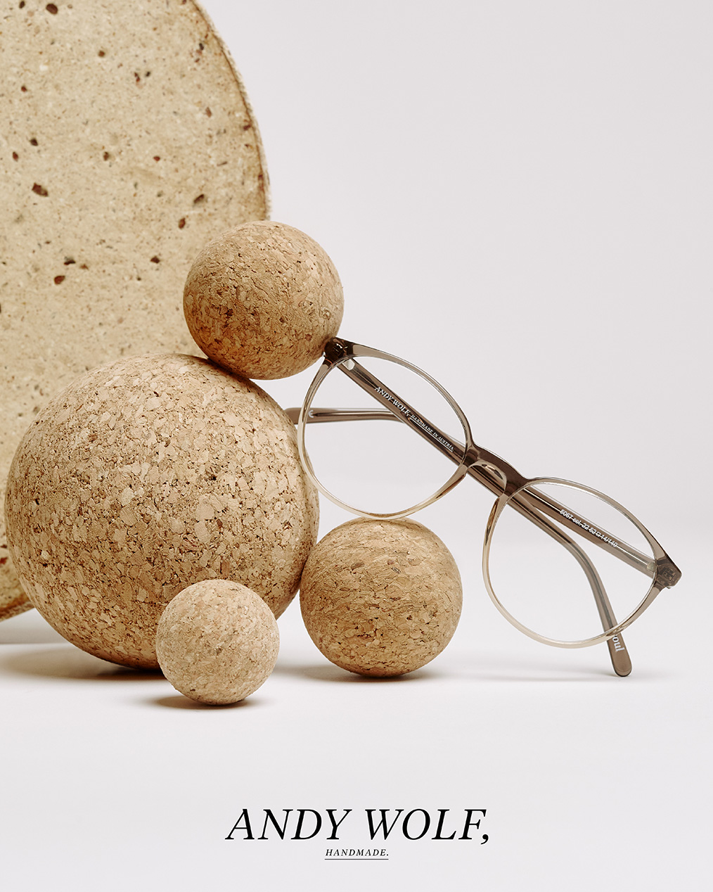 Brille mit grau-beigen Gestell von Andy Wolf liegt auf Korkbällen