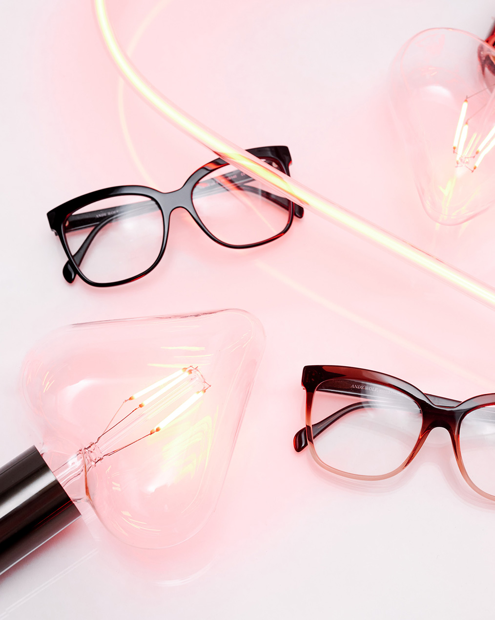 Zwei Brillenmodelle mit Schildplattmuster von Andy Wolf Berlin liegen in der Mitte eines rosanene LED-Schlauchs und herzförmigen Glühbirnen