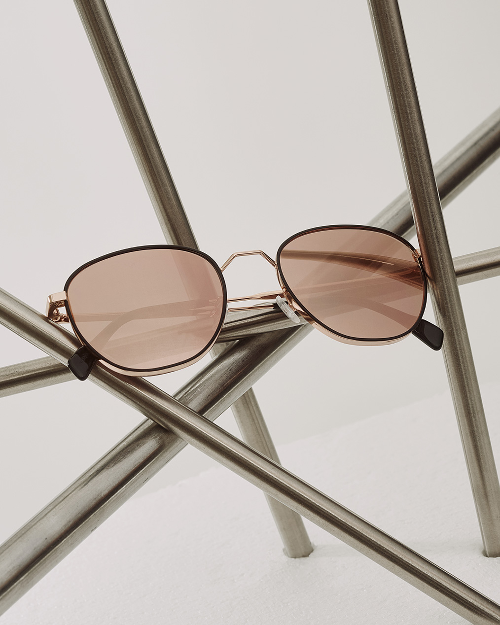 Sonnenbrille mit grau-rot getönten Gläsern von Andy Wolf liegt auf kunstvoll aufgestellten Chromestangen