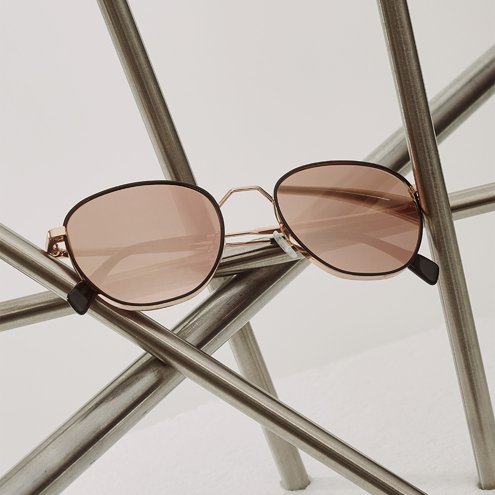 Sonnenbrille mit grau-rot getönten Gläsern von Andy Wolf liegt auf kunstvoll aufgestellten Chromestangen