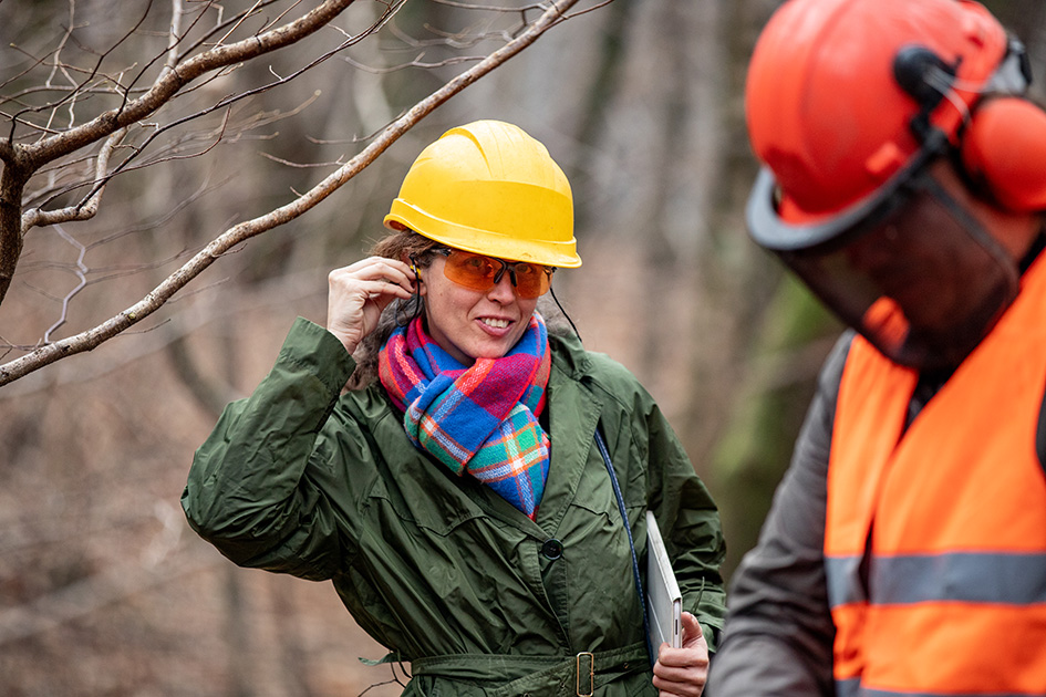 Eine Projektmanagerin und ein Baustellenmitarbiter mit verschiedenen Gehörschutz und Schutzhelmen auf der Baustelle