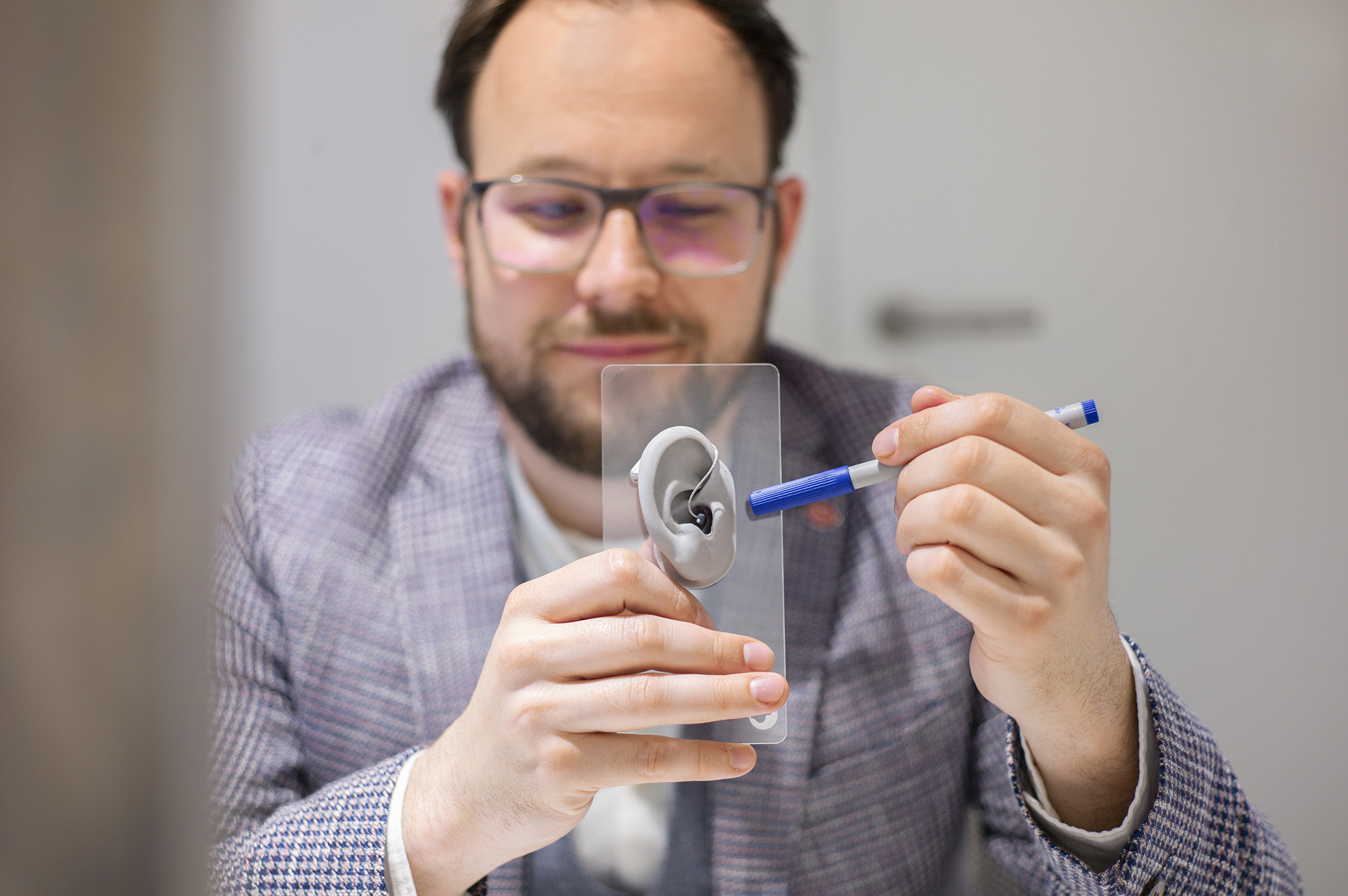 Hegle Garrels hält eine Modellplastik einer Ohrmuschel mit einem Hörgerät hoch und zeigt mit einem Stift auf den Empfängerteil