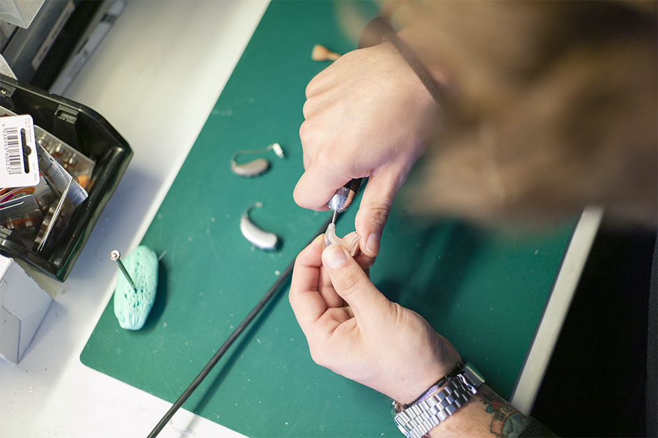 Draufsicht auf den Werktisch, an dem ein Mitarbeiter ein Hörgerät bearbeitet