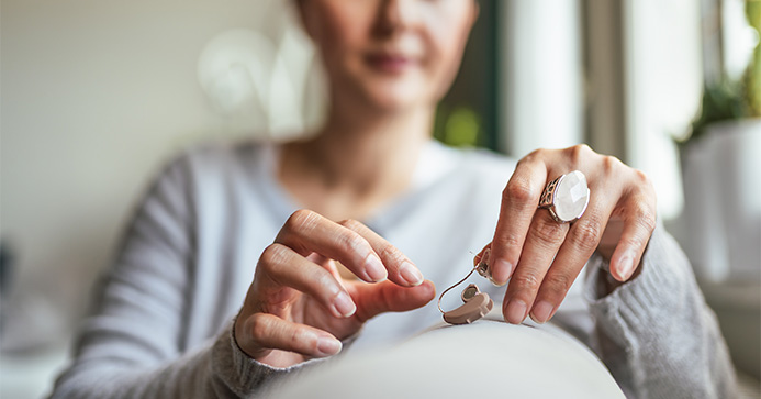 Frau auf Sofa wechselt die Batterie an ihrem Hörgerät