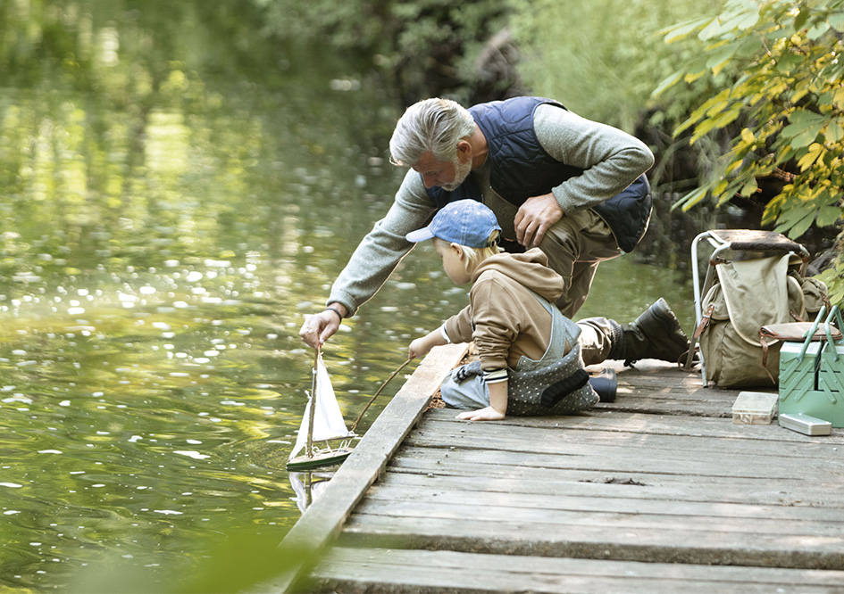 Großvater mit seinem kleinen Enkel auf einem Steg lassen ein kleines Spielsegelbot zu Wasser