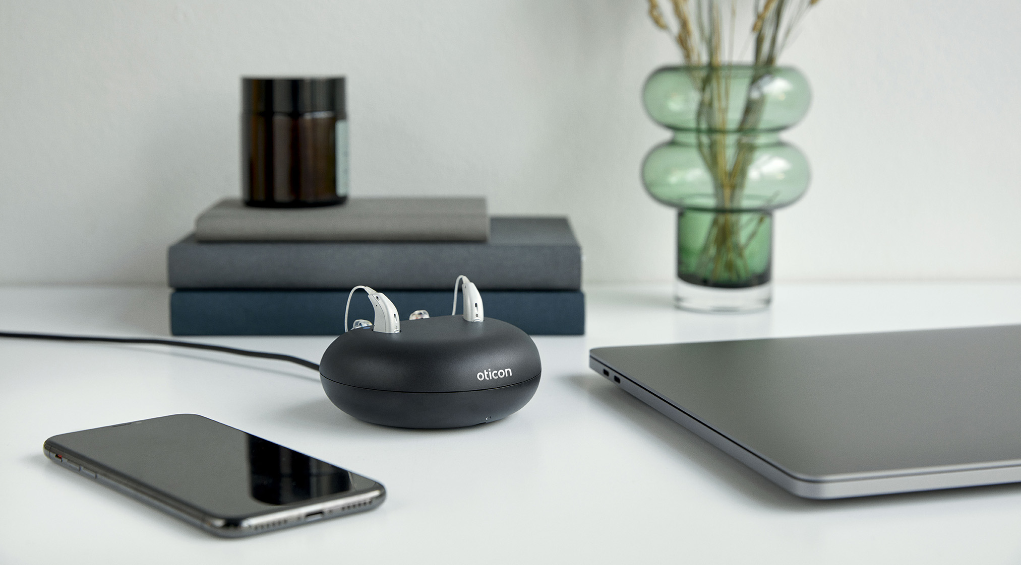 Tisch auf dem ein oticon-Ladegerät, ein Smartphone und ein Laptop liegen