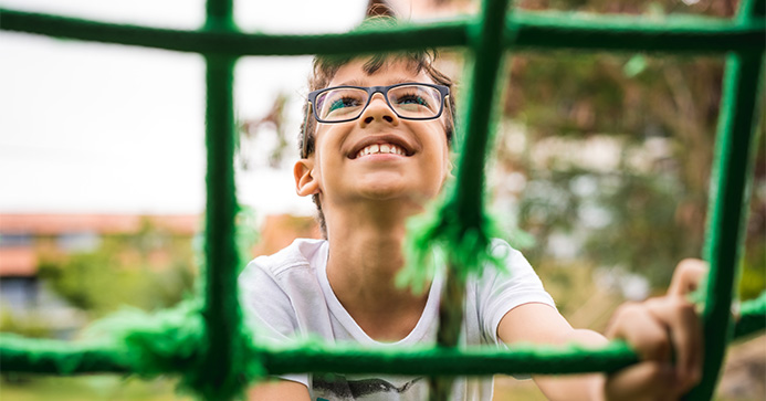 Junge mit Brille klettert auf ein Klettergerüst mit einem Seilnetz