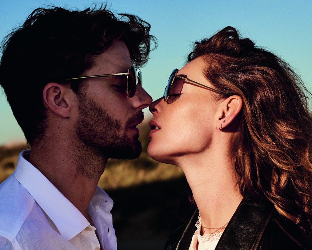 Pärchen mit Sonnenbrillen von Mexx küsst sich in der untergehenden Sonne