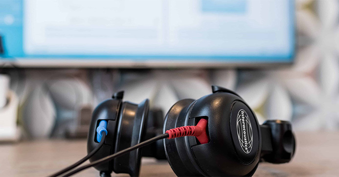 Kopfhörer für Hörtest liegen auf einem Tisch. Im Hintergrund ist unscharf ein Bildschirm mit der Testsoftware zu erkennen