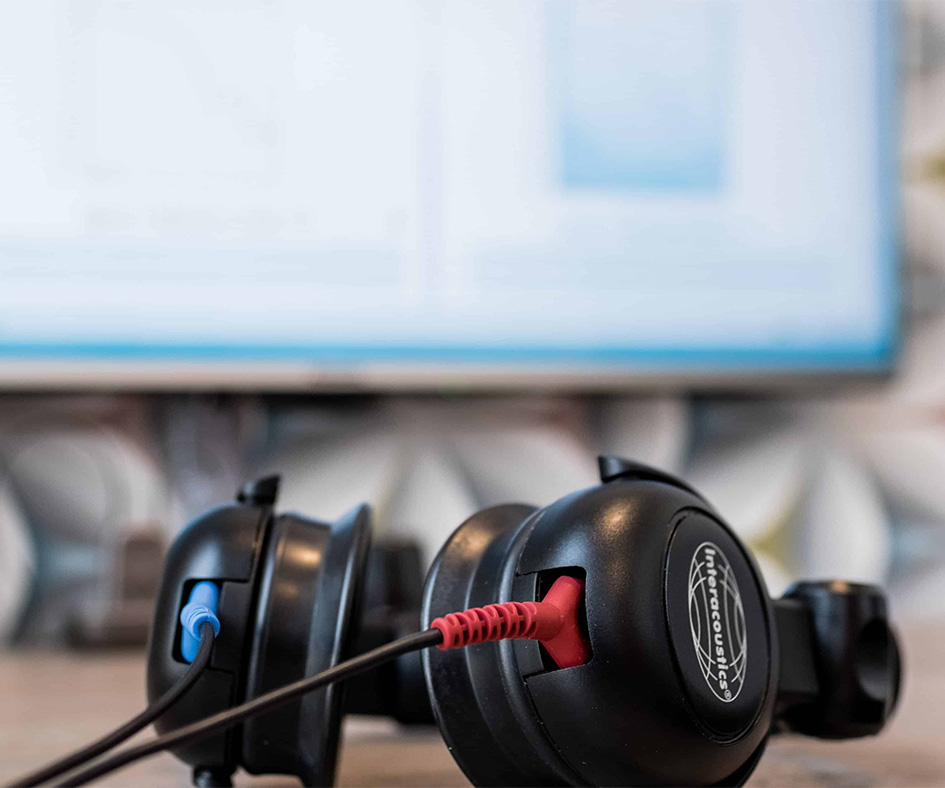 Kopfhörer für Hörtest liegen auf einem Tisch. Im Hintergrund ist unscharf ein Bildschirm mit der Testsoftware zu erkennen