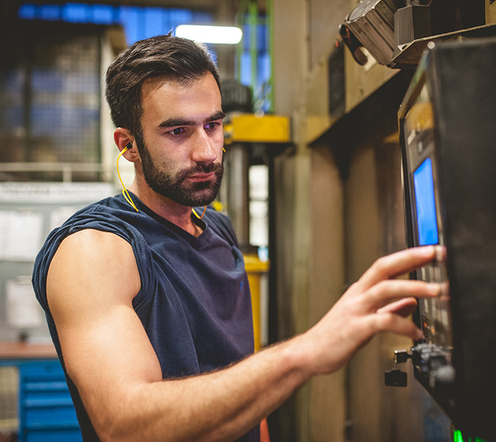 Mann in Werkhalle mit In-Ear-Gehörschutz bedient Maschine