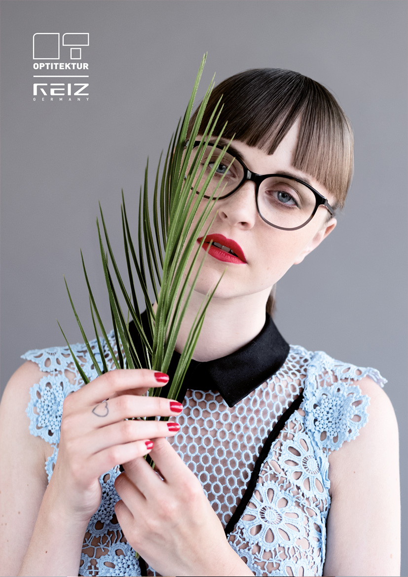 Junge Frau mit schwarze Brille von Reiz und roten Lippenstift hält einen Farn vor ihr Gesicht